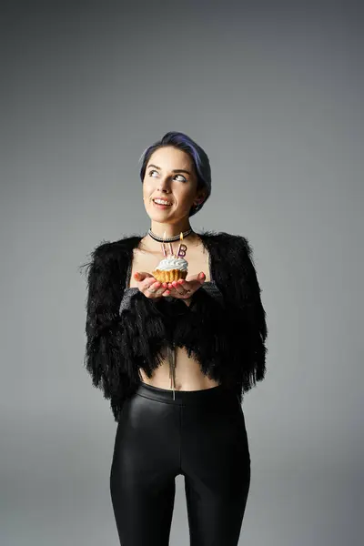 A stylish young woman in black attire holding a delicious cupcake with candles — Fotografia de Stock