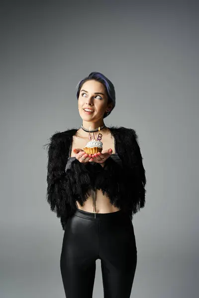 A stylish young woman in black attire holding a delicious cupcake with candles — Photo de stock