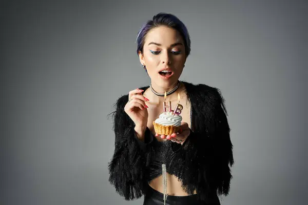 A young woman with short dyed hair strikes a pose while holding a delicious cupcake in a stylish outfit. — Photo de stock
