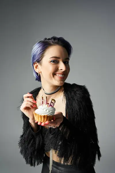 A young woman with vibrant blue hair holds a delicious cupcake in a stylish studio setting. — стокове фото