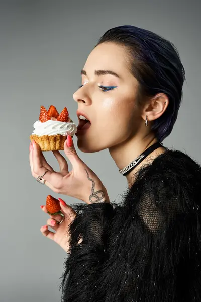 A fashionable young woman with short dyed hair enjoys a cupcake topped with strawberries in a studio setting. — Stock Photo