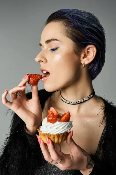 A young woman with vibrant blue hair enjoys a cupcake in a stylish studio setting. — стокове фото