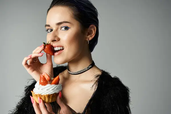 Young woman in black dress enjoying a cupcake with fresh strawberries — стокове фото