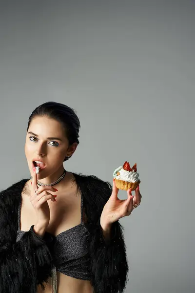 A stylish young woman with dyed hair poses with a cupcake, taking a bite from it. — стоковое фото