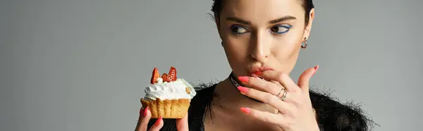 A young woman with dyed hair holding a cupcake in her right hand, exuding joy and celebration in stylish attire. — стокове фото