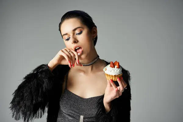 A stylish woman with short dyed hair poses while delicately holding a cupcake in a studio setting. — стоковое фото
