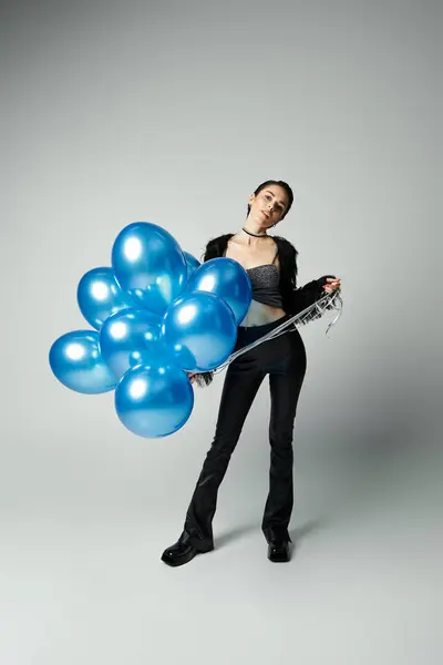 A vibrant young lady with chic style clutches a bunch of radiant blue balloons. — Stock Photo