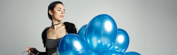 A young birthday girl with stylish attire holding a bunch of blue balloons in a studio setting. — Fotografia de Stock