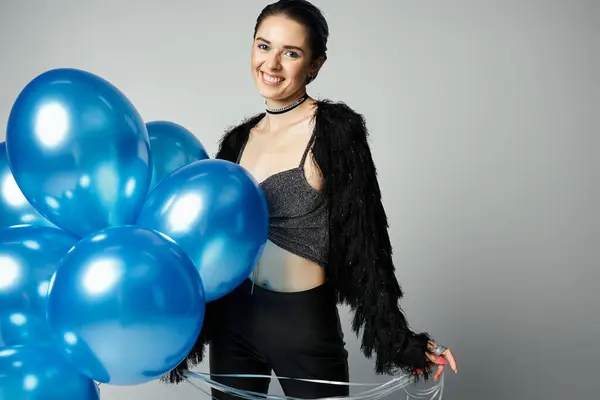 A young woman with short dyed hair smiling as she holds a bunch of blue balloons in a studio setting. — Photo de stock