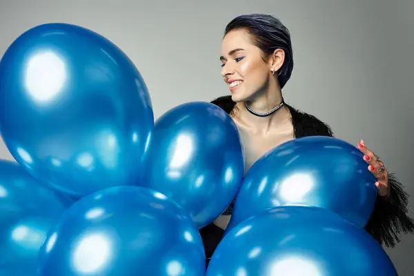 A pretty young woman with short dyed hair poses in stylish attire while holding a bunch of blue balloons. — Stock Photo