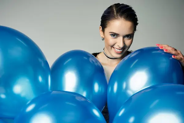 A young woman with short dyed hair joyfully holds a bunch of blue balloons in a stylish attire. - foto de stock