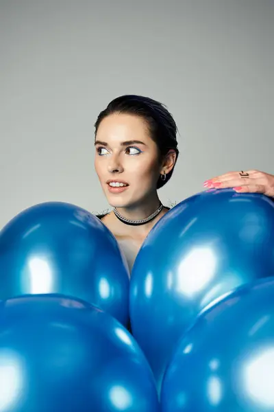 A trendy young woman with short dyed hair joyfully holds a bunch of vibrant blue balloons in a studio setting. — Stock Photo