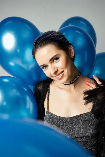 Young woman with short dyed hair poses stylishly in front of a backdrop of blue balloons. — Stock Photo