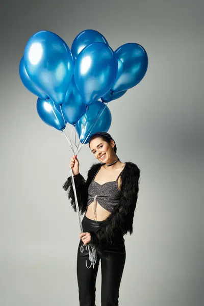A stylish young woman with short dyed hair holds a cluster of blue balloons in a studio setting. — стокове фото