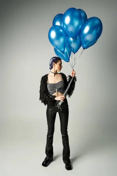 A young woman with short dyed hair holding a bunch of blue balloons, radiating joy and celebration in a studio setting. — Stock Photo