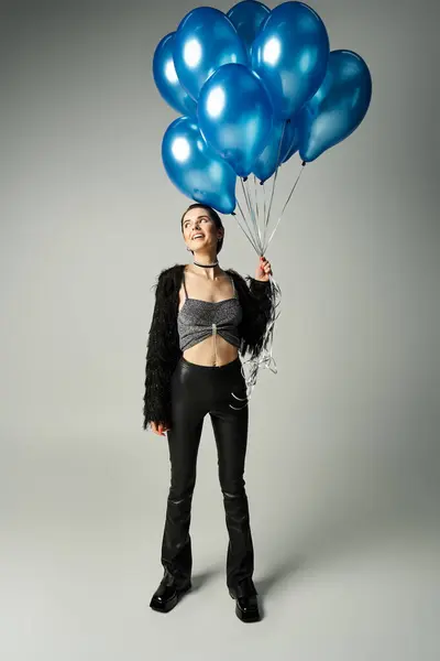 A stylish young woman with short dyed hair holding a bunch of blue balloons, exuding grace and joy. — Stock Photo
