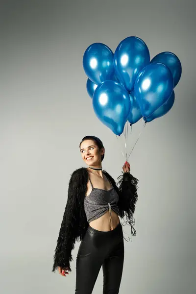 Young woman with short dyed hair smiles, holding a bunch of blue balloons in a stylish studio setting. — Stockfoto