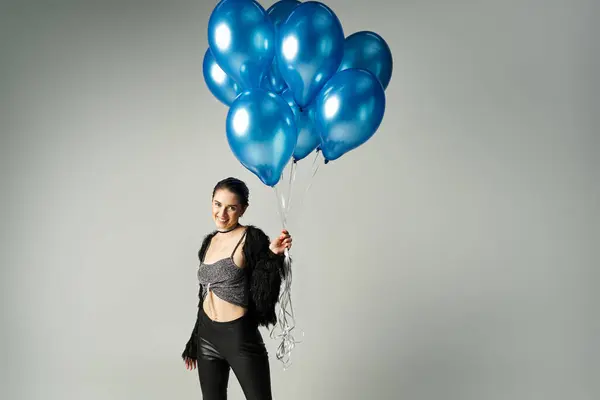 A stylish young woman, the birthday girl, smiling while holding a bunch of vibrant blue balloons. — Stock Photo