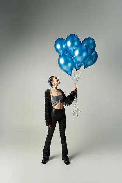 A vibrant woman with short dyed hair joyfully holds a bunch of blue balloons in a studio setting. — Photo de stock