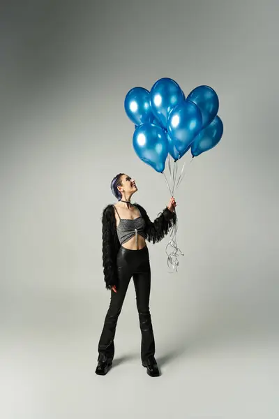 A vibrant woman with short dyed hair joyfully holds a bunch of blue balloons in a studio setting. — Stock Photo