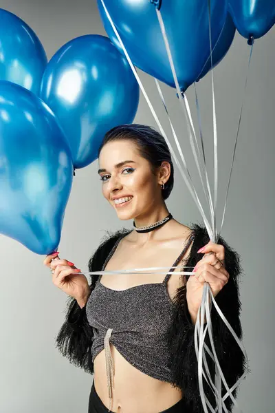 A stylish young woman with short dyed hair delightfully embraces a bunch of blue balloons in a studio setting. — Foto stock