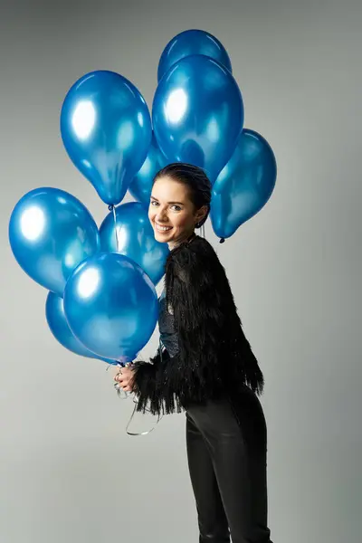 A stylish young woman with short dyed hair holding a bunch of bright blue balloons in a studio setting. — Stock Photo