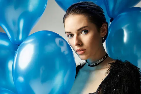 A young woman with short dyed hair holds a bunch of blue balloons, radiating joy and elegance in a studio setting. — Stockfoto