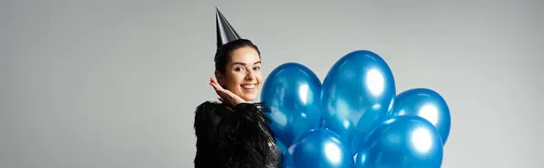 A stylish young woman with short dyed hair poses with a bunch of blue balloons in a studio setting. — Foto stock