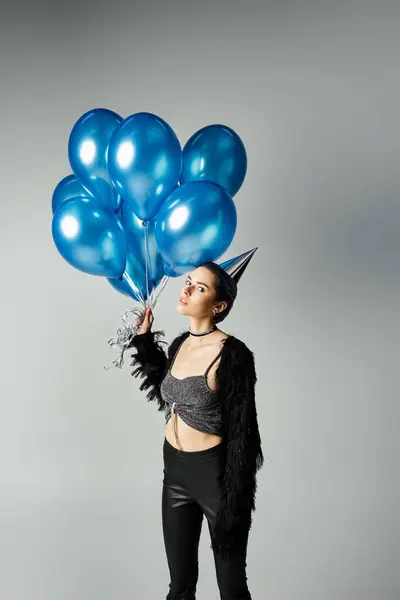 Short-haired young woman in chic attire joyfully holding a bunch of vibrant blue balloons in a studio setting. — стоковое фото