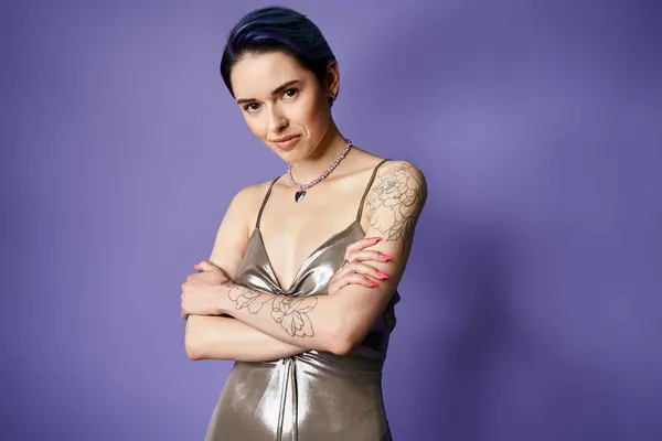 A pretty, young woman with short blue hair striking a pose in a shimmering silver dress in a studio setting. — Stockfoto