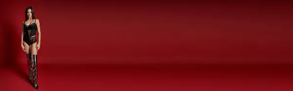 A woman in a black lingerie and wet hair standing confidently against a vibrant red background. — стоковое фото