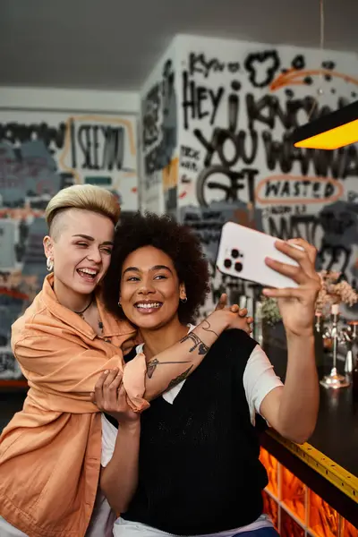 Deux belles lesbiennes capturent un moment dans un bar faiblement éclairé alors qu'elles prennent un selfie ensemble. — Photo de stock