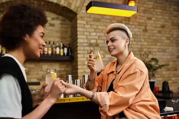 Diversa pareja de lesbianas disfrutando de una cita en un animado bar. - foto de stock