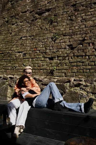 Deux femmes assises ensemble sur un banc devant un mur de pierre. — Photo de stock