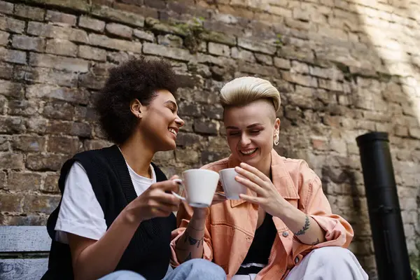 Two diverse women, a beautiful lesbian couple, relax and enjoy each others company on a bench. — Stock Photo