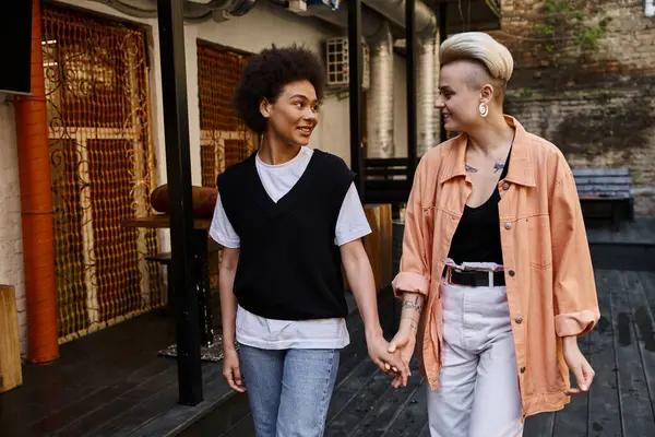 Разнообразная пара лесбиянок разделяет интимный момент, когда они идут по улице рука об руку. — стоковое фото