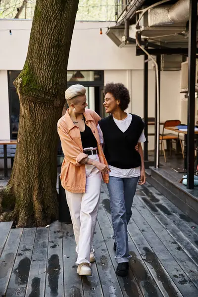 Two women peacefully walk next to a tree on a wooden walkway. — Stock Photo