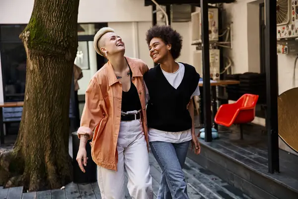 Two women casually walk alongside a tree on the sidewalk. — Stock Photo