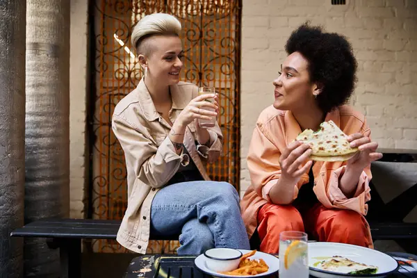 Zwei unterschiedliche, schöne Lesben sitzen an einem Tisch und genießen gemeinsam ein Essen. — Stockfoto