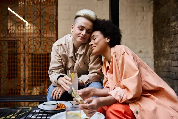 A diverse, beautiful lesbian couple enjoy a meal together at a cafe table. — Photo de stock