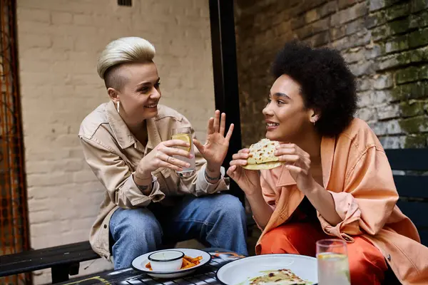 Zwei schöne Frauen verschiedener Ethnien sitzen zusammen an einem Tisch und teilen sich eine Mahlzeit in einem gemütlichen Café. — Stockfoto