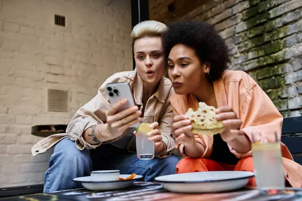 Diverse couple of lesbians sharing a moment with a cell phone in a cozy cafe. — Stock Photo