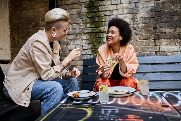 Разнообразная пара лесбиянок, сидящих за столом, наслаждающихся едой в уютном кафе. — стоковое фото