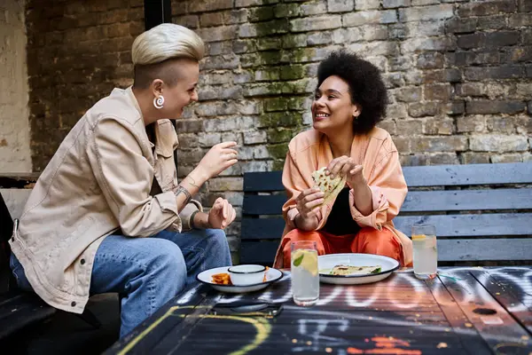 Una coppia eterogenea di lesbiche sedute a un tavolo, che si godono un pasto in un accogliente caffè. — Foto stock
