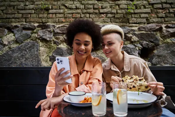 Um casal diversificado de mulheres desfrutando de uma refeição juntas em uma mesa em um café. — Fotografia de Stock