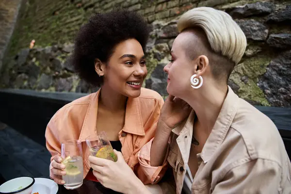 Two diverse women enjoy a date at a cozy cafe, sitting close and engaged in conversation. — Stock Photo