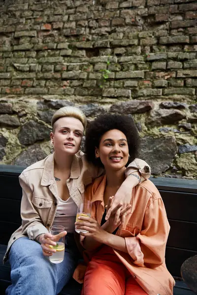 Couple de lesbiennes profitant de boissons ensemble sur un banc dans un café. — Photo de stock
