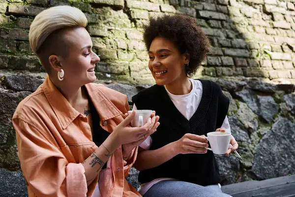 Two diverse women sitting closely, engaged in conversation in a cozy cafe setting. — Stock Photo