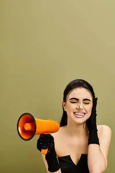Brünette Frau in schwarzem Kleid und Handschuhen hält leuchtendes gelb-oranges Megafon im Pop-Art-Make-up-Stil. — Stockfoto