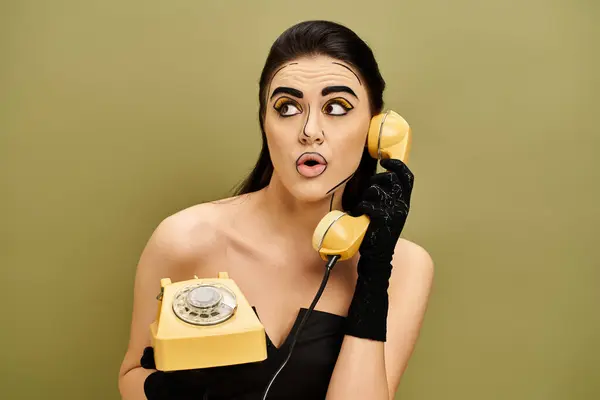 A fashionable brunette woman in a black dress and gloves, holding a yellow retro telephone. — Stock Photo